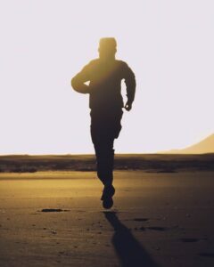 silhouette of unrecognizable man running on sand at sunset